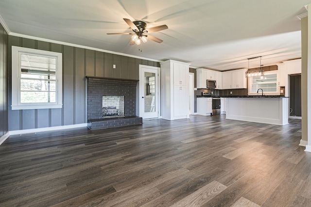 unfurnished living room with sink, a brick fireplace, ceiling fan, crown molding, and dark hardwood / wood-style floors