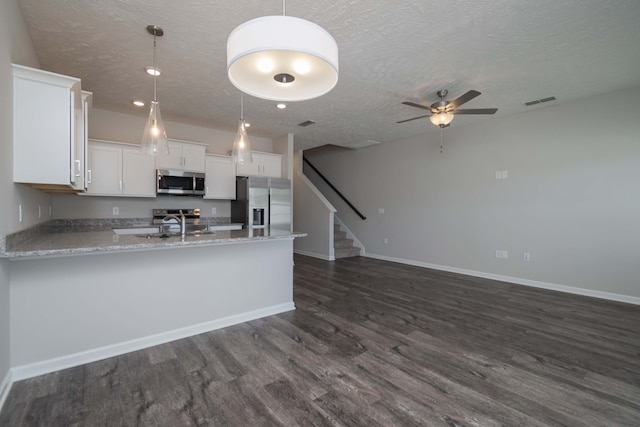 kitchen with appliances with stainless steel finishes, a textured ceiling, hanging light fixtures, white cabinets, and dark wood-type flooring