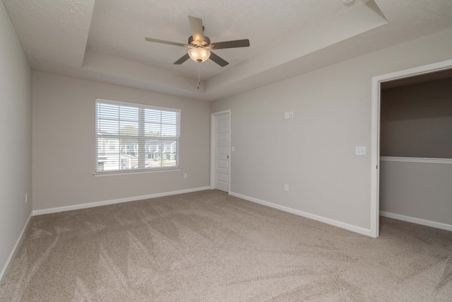 carpeted empty room with ceiling fan and a raised ceiling