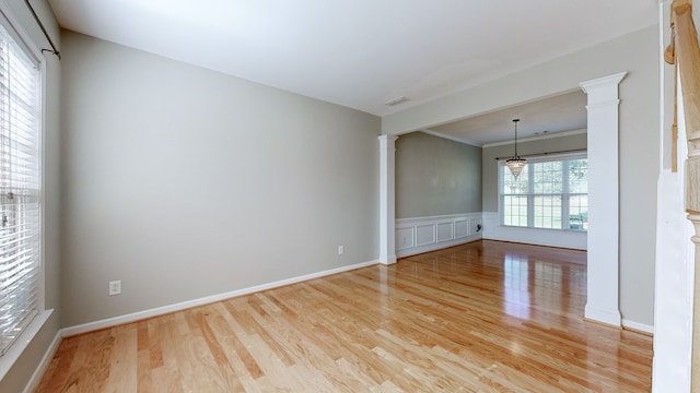 empty room featuring light hardwood / wood-style floors, crown molding, an inviting chandelier, and decorative columns