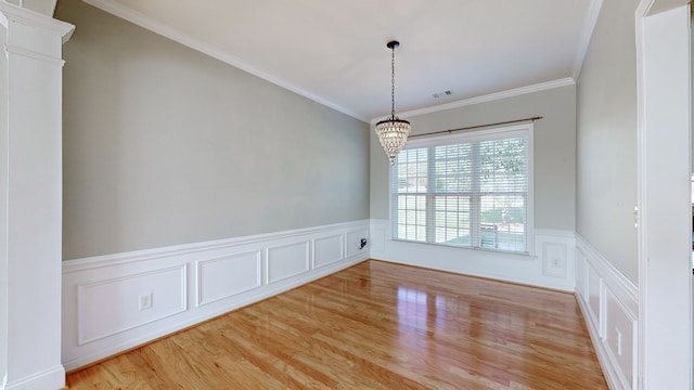 empty room with decorative columns, light hardwood / wood-style floors, ornamental molding, and an inviting chandelier