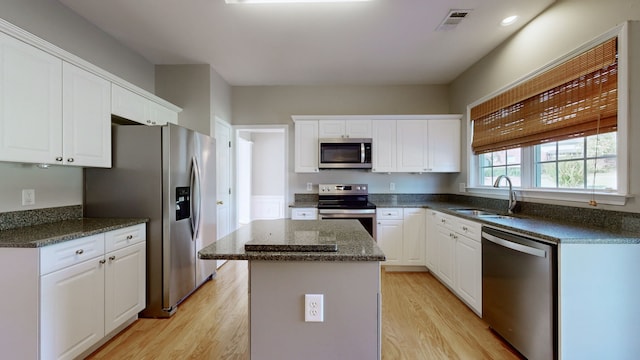 kitchen featuring appliances with stainless steel finishes, sink, light wood-type flooring, a center island, and white cabinets