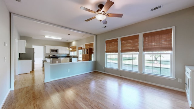 kitchen with kitchen peninsula, stainless steel appliances, decorative light fixtures, white cabinets, and light hardwood / wood-style flooring