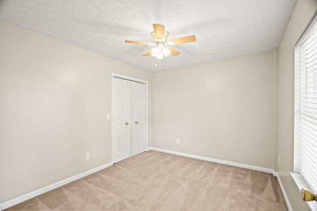 unfurnished bedroom featuring a closet, ceiling fan, a textured ceiling, and light colored carpet