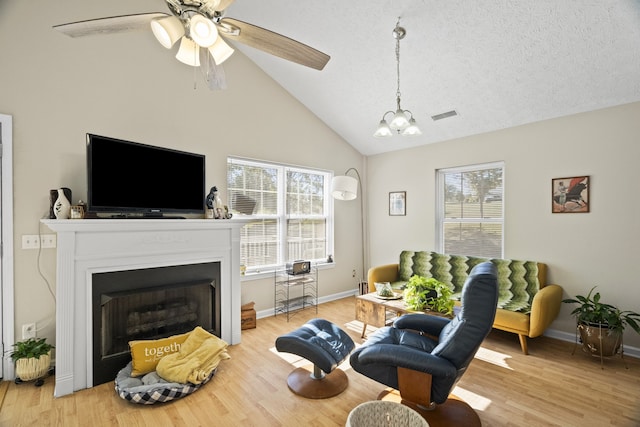 living room with high vaulted ceiling, a textured ceiling, light wood-type flooring, and ceiling fan with notable chandelier