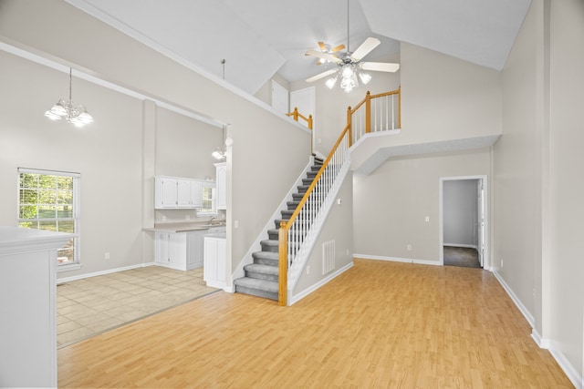 unfurnished living room with light hardwood / wood-style floors, ceiling fan with notable chandelier, and high vaulted ceiling