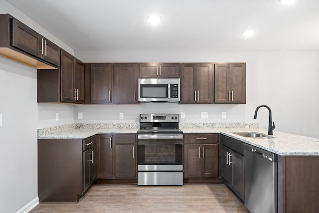 kitchen featuring dark brown cabinets, light stone countertops, light wood-type flooring, sink, and stainless steel appliances