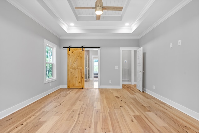 unfurnished bedroom with crown molding, a barn door, light hardwood / wood-style floors, and a raised ceiling