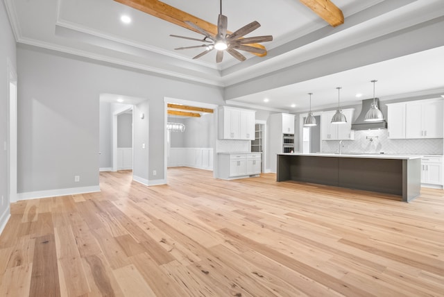 unfurnished living room with beam ceiling, a tray ceiling, light hardwood / wood-style flooring, ornamental molding, and ceiling fan with notable chandelier