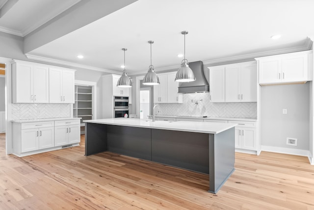 kitchen featuring wall chimney exhaust hood, a center island with sink, and white cabinets