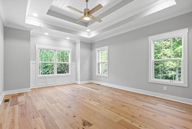 empty room featuring crown molding, a raised ceiling, a wealth of natural light, and light hardwood / wood-style floors