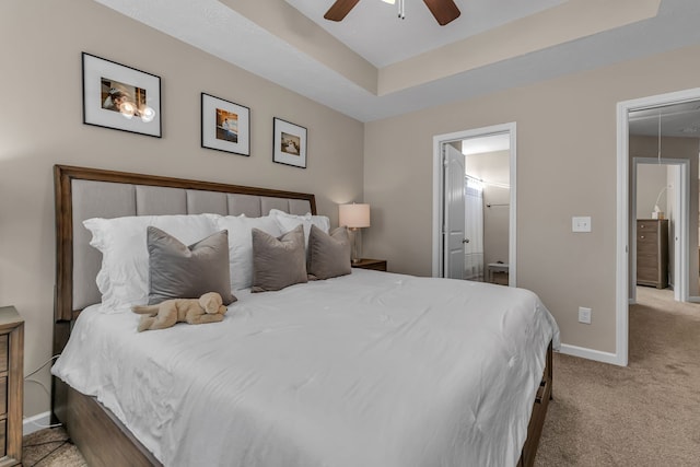 carpeted bedroom featuring ceiling fan, a tray ceiling, and ensuite bathroom