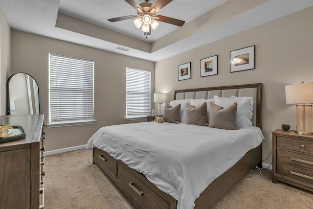 carpeted bedroom with ceiling fan and a tray ceiling