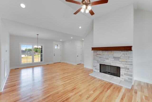 unfurnished living room with light hardwood / wood-style flooring, a stone fireplace, high vaulted ceiling, and ceiling fan with notable chandelier