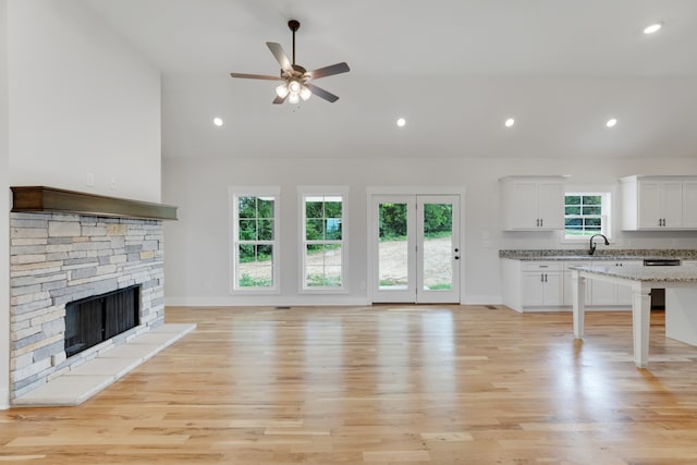 unfurnished living room featuring high vaulted ceiling, a stone fireplace, light hardwood / wood-style flooring, and ceiling fan