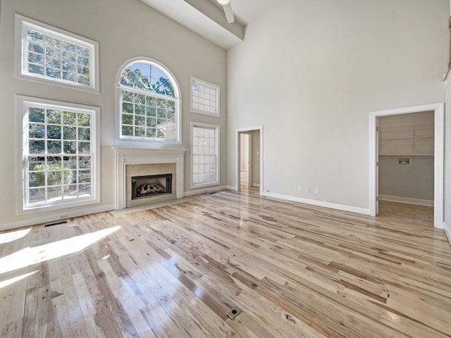 unfurnished living room with a premium fireplace, a high ceiling, light wood-type flooring, and ceiling fan