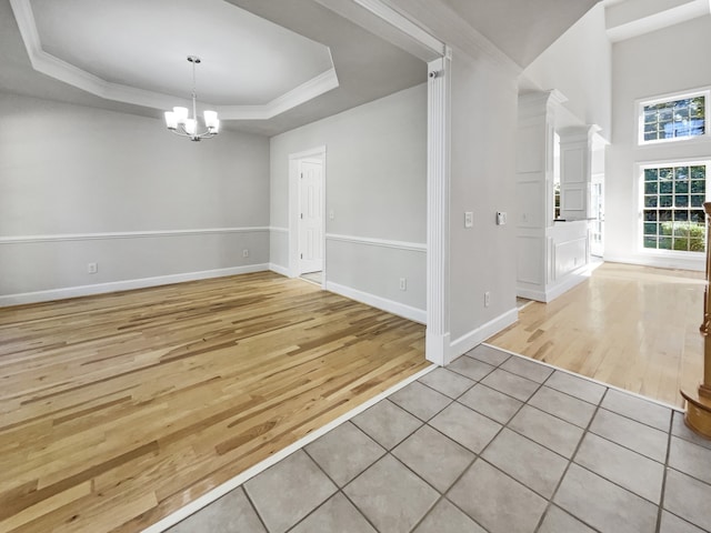 empty room with light hardwood / wood-style floors, a raised ceiling, an inviting chandelier, and crown molding