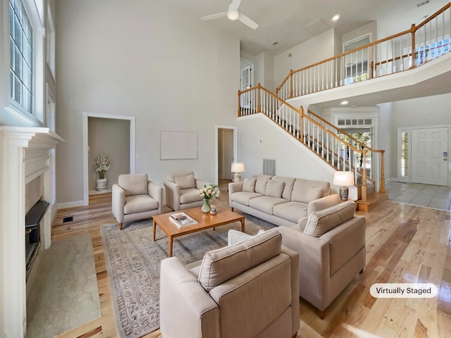 living room with ceiling fan, a high ceiling, and light wood-type flooring