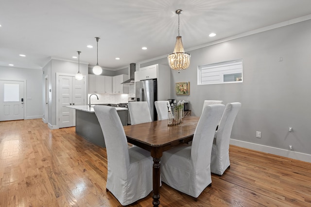 dining area with sink, crown molding, light hardwood / wood-style flooring, and an inviting chandelier