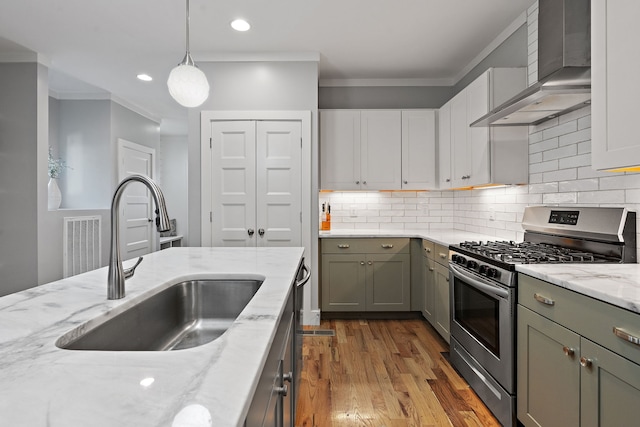 kitchen featuring wall chimney range hood, gas range, light hardwood / wood-style flooring, sink, and decorative light fixtures