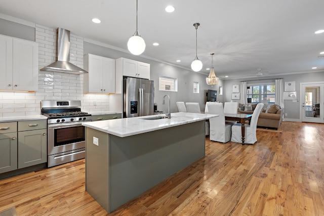 kitchen featuring wall chimney range hood, an island with sink, sink, appliances with stainless steel finishes, and light hardwood / wood-style floors