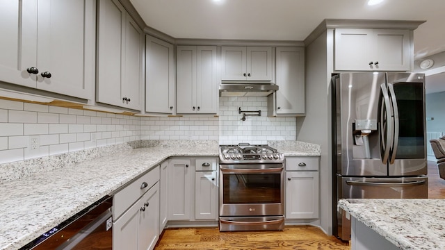 kitchen featuring gray cabinetry, light stone countertops, appliances with stainless steel finishes, light wood-type flooring, and decorative backsplash