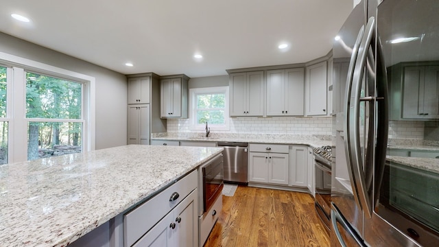 kitchen with appliances with stainless steel finishes, light stone counters, wood-type flooring, and backsplash