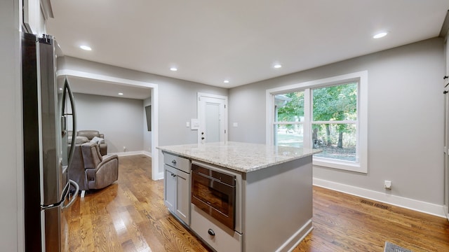 kitchen with gray cabinetry, a kitchen island, light hardwood / wood-style floors, stainless steel appliances, and light stone counters