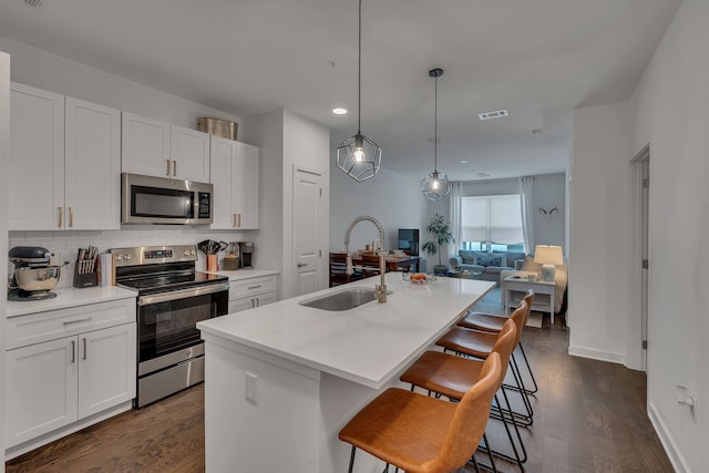 kitchen with a kitchen island with sink, stainless steel appliances, sink, pendant lighting, and white cabinets