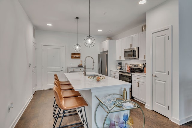 kitchen featuring a kitchen island with sink, dark wood-type flooring, stainless steel appliances, pendant lighting, and white cabinetry