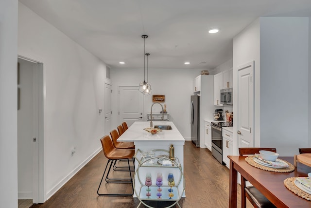 kitchen with sink, stainless steel appliances, decorative light fixtures, white cabinets, and a kitchen island with sink