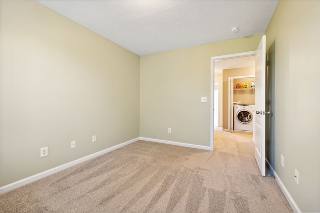 unfurnished room with light carpet, washer / dryer, baseboards, and a textured ceiling