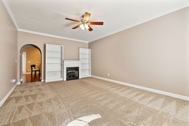 unfurnished living room featuring arched walkways, a fireplace, light colored carpet, and crown molding