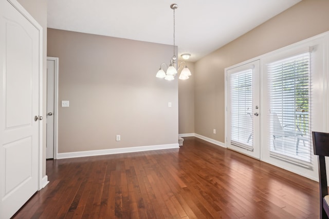 spare room with dark wood-style floors, baseboards, and an inviting chandelier