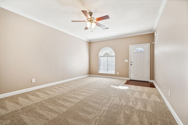 carpeted foyer entrance with ornamental molding, a ceiling fan, visible vents, and baseboards