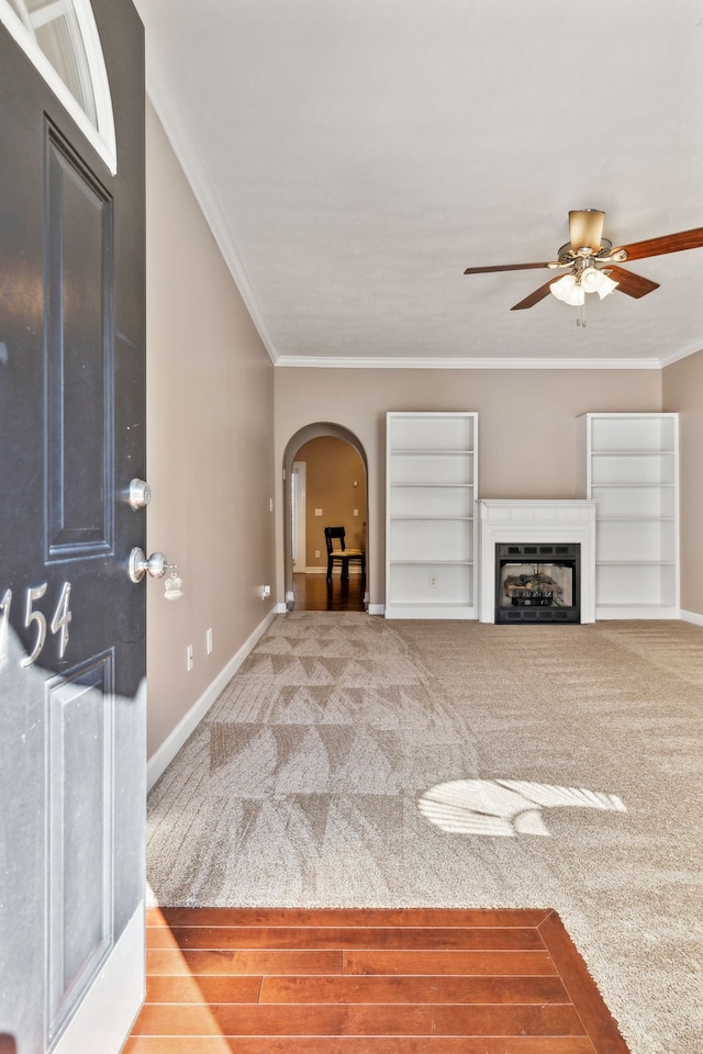 unfurnished living room featuring carpet floors, arched walkways, a fireplace, crown molding, and baseboards