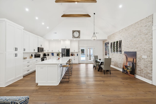 kitchen with white cabinetry, wood-type flooring, beamed ceiling, and a center island with sink