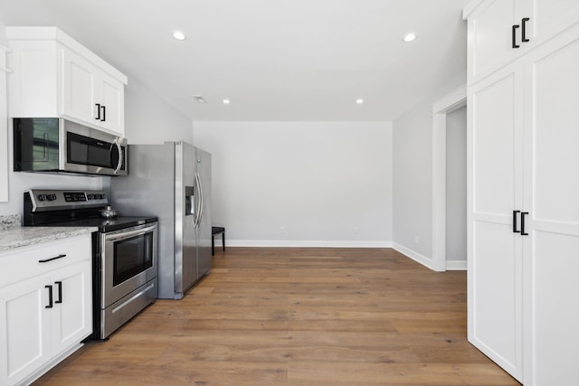 kitchen featuring appliances with stainless steel finishes, white cabinetry, light stone counters, and light wood-type flooring