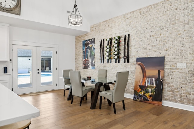 dining space featuring french doors, hardwood / wood-style floors, a notable chandelier, and brick wall