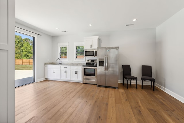 kitchen featuring light stone countertops, white cabinetry, stainless steel appliances, and light hardwood / wood-style floors