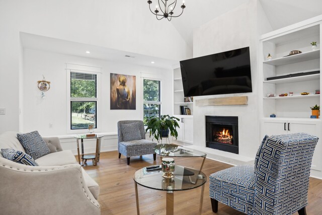 living room with high vaulted ceiling, hardwood / wood-style flooring, a chandelier, and built in shelves