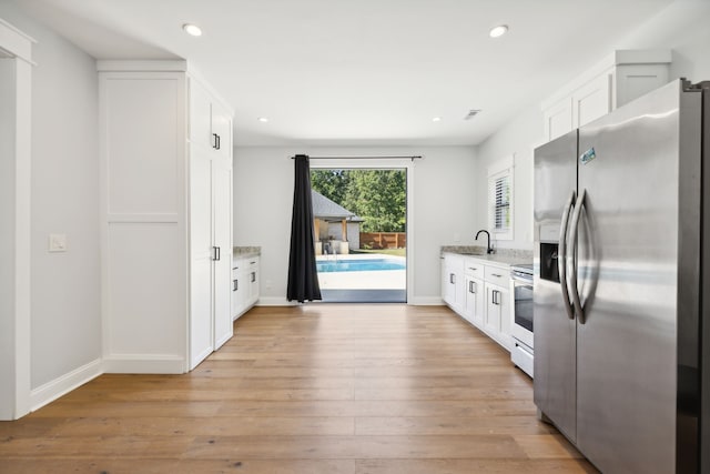 kitchen with light hardwood / wood-style flooring, electric range, stainless steel fridge with ice dispenser, white cabinets, and light stone counters