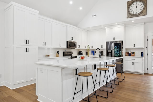 kitchen featuring appliances with stainless steel finishes, a kitchen island with sink, white cabinets, and light hardwood / wood-style floors