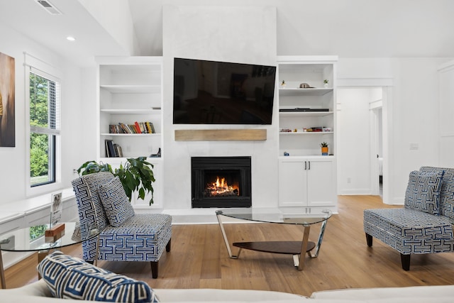 living room featuring vaulted ceiling, light hardwood / wood-style floors, and a large fireplace