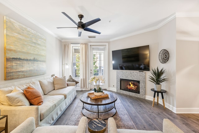 living room featuring ceiling fan, a tiled fireplace, ornamental molding, and hardwood / wood-style floors