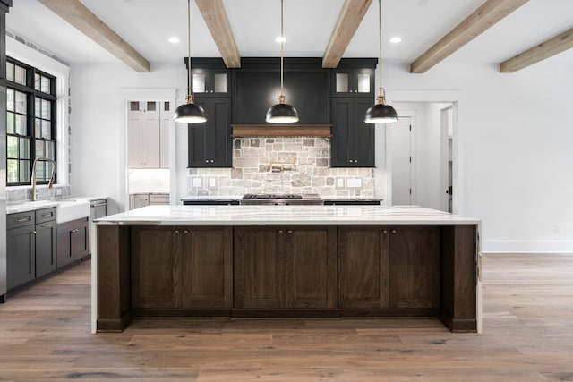 kitchen featuring light stone countertops, a spacious island, dark hardwood / wood-style flooring, beamed ceiling, and decorative backsplash