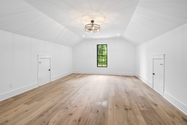 additional living space featuring vaulted ceiling, a notable chandelier, and light wood-type flooring