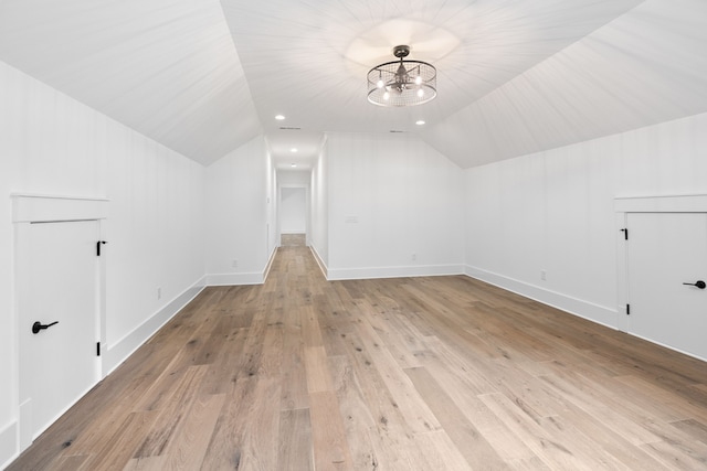 additional living space featuring an inviting chandelier, vaulted ceiling, and light wood-type flooring