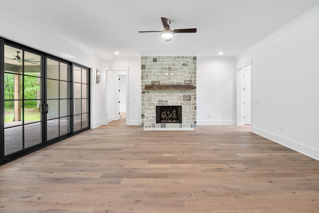 unfurnished living room featuring light hardwood / wood-style floors, a stone fireplace, crown molding, and ceiling fan