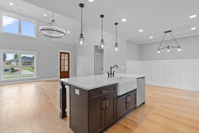 kitchen featuring a towering ceiling, sink, dishwasher, decorative light fixtures, and light hardwood / wood-style flooring